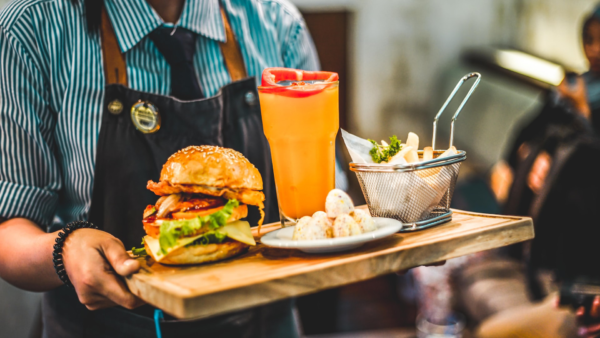 Restaurant server holding a tray of burger, apps and a drink. They
