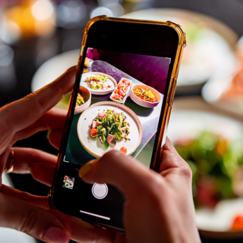 Hand holding a smartphone taking photos of restaurant menu specials for Instagram marketing